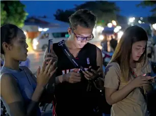  ?? AP ?? People check their mobile phones for update while waiting at a military airbase during emergency helicopter evacuation in Chiang Rai province, northern Thailand, on Monday —