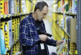  ?? MARK LENNIHAN — THE ASSOCIATED PRESS ?? In this Wednesday photo, a clerk picks an item from a shelf and scans it with a hand-held device to fill a customer order at the Amazon Prime warehouse in New York.