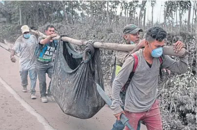  ?? Picture: AP. ?? Men carry a body near Volcan de Fuego, or “Volcano of Fire”, in Escuintla.