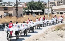  ?? Karam Al-Masri AFP/Getty Images ?? MEMBERS of the Syrian Red Crescent transport the bodies of soldiers from a rebel-held area to a government-held area of Aleppo last week.