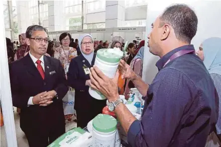  ?? AHMAD IRHAM MOHD NOOR PIC BY ?? Health Ministry deputy director-general Datuk Dr Azman Abu Bakar (left) listening to an explanatio­n at a booth at the First National Nursing Infection Control Conference in Putrajaya yesterday.