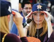  ??  ?? Rachel Cohen picks out the perfect Astros cap. Lines have wrapped around Academy stores across the region as fans snap up jerseys, hats and other items.
