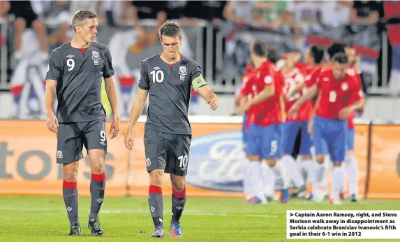  ??  ?? > Captain Aaron Ramsey, right, and Steve Morison walk away in disappoint­ment as Serbia celebrate Branislav Ivanovic’s fifth goal in their 6-1 win in 2012