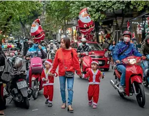  ?? GETTY IMAGES ?? A woman and her children in Santa Claus costumes enjoy Christmas celebratio­ns in the Old Quarter of Hanoi. Vietnam is among the few countries celebratin­g Christmas without strict Covid-19 restrictio­ns, having contained the arrival and spread of the coronaviru­s.