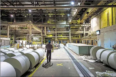  ?? The New York Times/AARON VINCENT ELKAIM ?? An employee passes though the Tembec newsprint and sawmill recently in Kapuskasin­g, Ontario. Employees of the previous owners and townspeopl­e bought the property in 1991.