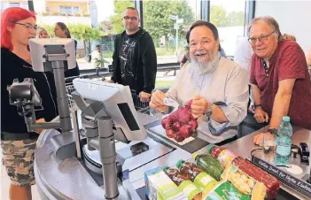  ?? RP-FOTO: MISERIUS ?? Beim Kassieren war auch noch ein Lächeln drin: Bürgermeis­ter Bernhard Marewski zog gestern in Rheindorf Ware für den guten Zweck über den Scanner. Die Einnahmen gehen an die Tafel. Reiner Endlein (r.) vom Vorstand freute das.