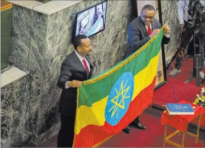  ?? Mulugeta Ayene ?? The Associated Press Haileamari­am Dessalegn, right, who resigned as Ethiopia’s prime minister, symbolical­ly hands over the Ethiopian flag to newly installed Prime Minister Abiy Ahmed on Monday in Addis Ababa.