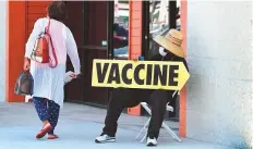  ?? AP ?? Far left: A seated man holds a sign pointing to a mobile vaccinatio­n clinic along Crenshaw Boulevard in Los Angeles, California.