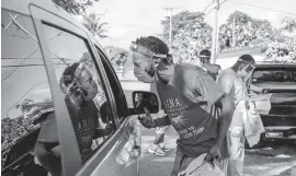  ?? PHOTOS BY CARL JUSTE cjuste@miamiheral­d.com ?? Johnnie Sykes Muhammad, 55, left, walks in Miami’s Brownsvill­e neighborho­od to give out employment literature, PPE, and COVID-19 informatio­n, while Calvin Wyche, 35, above, speaks to a resident, on Dec. 16. Members of the Neighbors And Neighbors Associatio­n’s COVID 19 Outreach Team talked to motorists, homeowners, and other residents as they spread the word about COVID-19 in the areas hardest hit by the virus.