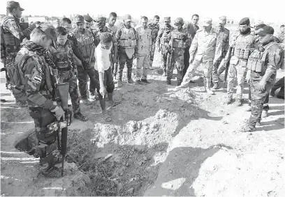  ?? — Gambar AFP ?? TERBIAR: Anggota tentera dan wartawan meninjau salah satu kubur beramai-ramai yang disyaki mengandung­i rangka mangsa IS dekat bekas pangkalan tentera Al-Bakara di barat daya Hawija, kelmarin.