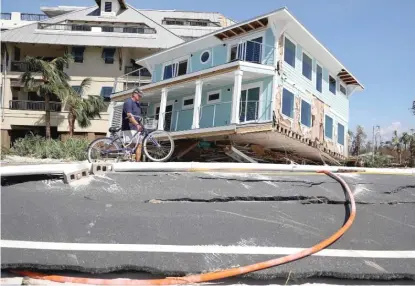  ?? JOE RAEDLE/GETTY IMAGES ?? A man walks his bike Thursday past a home that was carried across a road and slammed up against a condo complex in Mexico Beach, Florida, when Hurricane Michael came ashore Wednesday with winds measured at 155 mph.