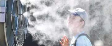  ??  ?? A spectator stands in front of a mist fan on day four of the Australian Open tennis tournament in Melbourne. — AFP photo