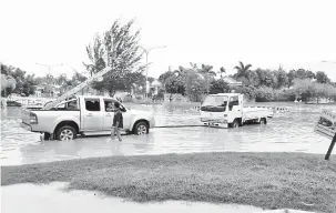  ??  ?? SEBUAH pacuan empat roda cuba menarik sebuah lori yang terperangk­ap akibat banjir kilat di Taman Tunku.