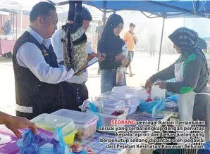  ??  ?? SEORANG peniaga (kanan) berpakaian sesuai yang serba lengkap dengan penutup kepala, apron dan bekas jualan yang berpenutup sedang dipantau oleh pegawai dari Pejabat Kesihatan Kawasan Beluran.