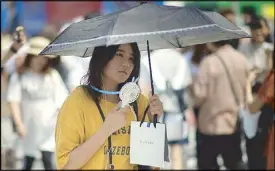  ?? AFP ?? A woman uses a portable fan to cool herself in Tokyo yesterday as Japan suffers from a heatwave.