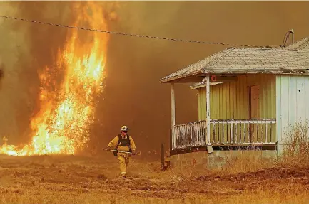  ?? PHOTO: REUTERS ?? A firefighte­r walks near a home as flames from the fast-moving Detwiler fire approach in Mariposa, California,