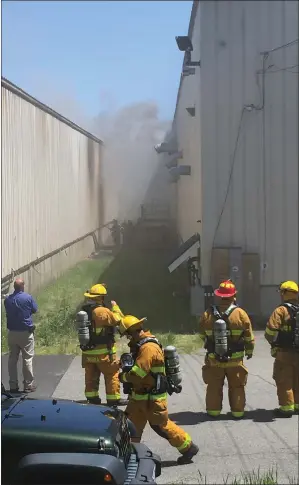  ??  ?? RIGHT: A group of firefighte­rs in the foreground look on as another group approach an area of heavy smoke on Monday outside the Boukaert Industrial Textiles facility on Privilege Street in Woonsocket.