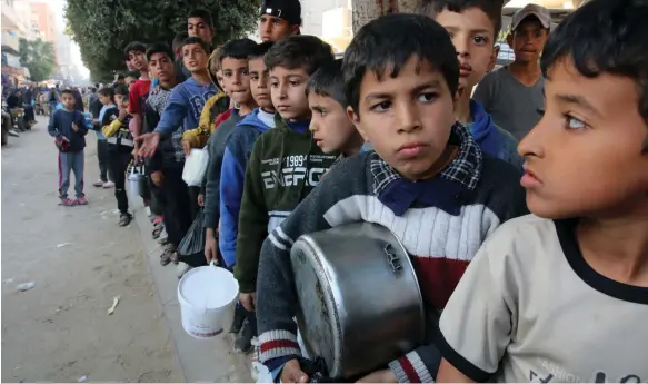  ?? Bloomberg ?? Children queue for food at a street kitchen in Deir Al Balah, central Gaza, amid growing hunger in the besieged Palestinia­n enclave