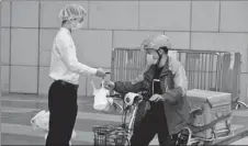  ?? ZHAO RUIXI / XINHUA ?? A restaurant employee (left) hands over a food parcel to a Ele.me deliveryma­n outside a shopping center in Shenzhen, Guangdong province, on March 12.