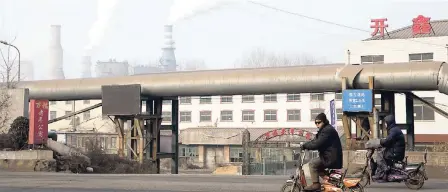  ?? FILE ?? In this photo taken Friday, December 30, 2016, a man rides a bike past smoke spewing from the sprawling complex that is a part of the coal-powered Jiujiang steel and rolling mills in Qianan in northern China’s Hebei province.