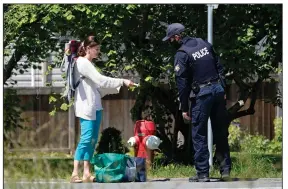  ?? (AP/Elaine Thompson) ?? A Royal Canadian Mounted Police officer on Tuesday checks the identifica­tion of a woman who had just walked back into Canada by crossing a small ditch from Peace Arch Historical State Park in Blaine, Wash. The border has been closed to nonessenti­al travel since March 2020, but Canadians have been allowed to cross the ditch into the U.S. park.