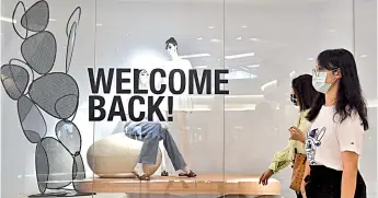  ?? File photo — AFP ?? Women walk past a clothing store’s display window with a ‘Welcome Back!’ sign in a shopping mall in Bangkok as sectors of the economy are being reopened following restrictio­ns to halt the spread of the Covid-19 coronaviru­s.