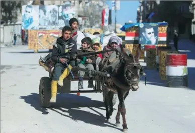  ?? ALI HASHISHO / REUTERS ?? Children ride a donkey cart along a street in Aleppo, Syria, on Thursday. Pictures of Syria's President Bashar al-Assad are seen in the background.