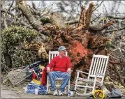  ??  ?? Steven West takes a break in front of a large tree that was toppled between his home and his relatives’ house next door by the fierce storms that lashed Coweta County.