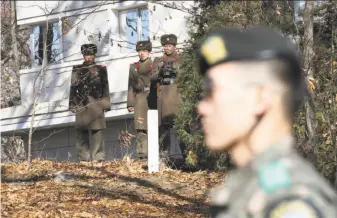  ?? Lee Jin-Man / Associated Press ?? North Korean soldiers (at rear) stand guard as a South Korean soldier passes near where a North Korean soldier crossed the border on Nov. 13 in the the Demilitari­zed Zone.