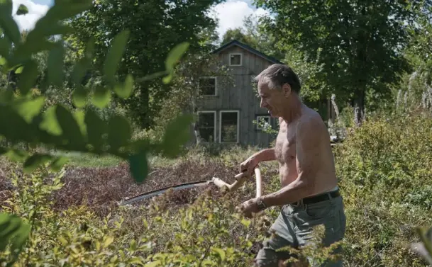  ??  ?? Heinrich cuts brush with a scythe, one of the many physical jobs he does to maintain his 600 acres. He does not seem to mind the hard labour