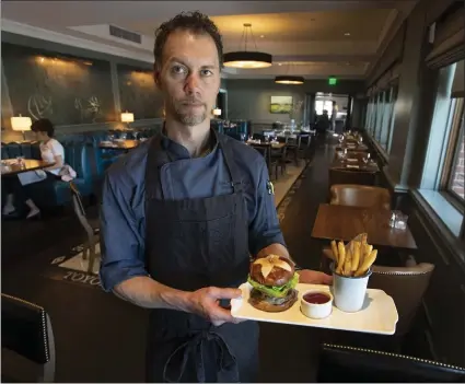  ?? PHOTOS BY KARL MONDON — STAFF PHOTOGRAPH­ER ?? Jason Dalling, executive chef of Menlo Tavern inside the Stanford Park Hotel, shows off the Tavern Burger, Harris Ranch Black Angus beef on a pretzel bun.