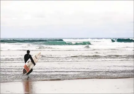  ?? KRISTIAN CARREON ?? A surfer heads out at Mission Beach on a cloudy Thursday afternoon. The same conditions are expected through the weekend.