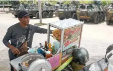  ?? — AFP photo ?? A hawker cooks up meatball soup beside police armoured vehicles parked near the venue of the G20 Bali Summit in Nusa Dua, Bali.