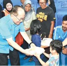  ?? ?? Uggah hands out packed food to a child at Dewan Sinaran Sungai Lumut temporary relief centre.