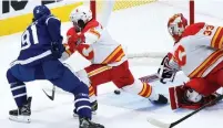  ?? NATHAN DENETTE THE CANADIAN PRESS ?? Calgary goaltender David Rittich, right, makes a stick save on a shot by Toronto centre John Tavares, left, as he’s being checked by Flames defenceman Rasmus Andersson Monday night in Toronto. For full coverage of Monday’s game, visit thespec.com.