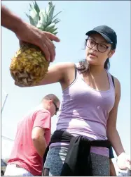  ?? RECORDER PHOTO BY CHIEKO HARA ?? Volunteer Krystal Torres hands out a pineapple Friday, Aug. 24, 2018 at Neighborho­od Market, presented by Burton School District. They provide seasonal food items to the community members in every fourth Friday of the month.