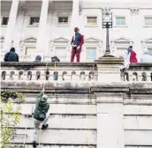  ?? JASON ANDREW/THE NEW YORK TIMES ?? A man climbs a wall at the U.S. Capitol during the Jan. 6 riot. To date, 32 riot-related prison sentences have been handed down.