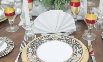  ??  ?? The table is set for the holidays with gold charger plates, crimson and gold stemware and linen napkin fans.