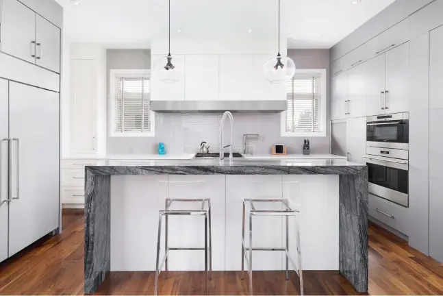  ??  ?? Dual-tone cabinets exhibit a combinatio­n of slab and Shaker door styles in muted hues of white and grey. The hood fan captures flanking cabinetry with a stainless steel trim. Island features include a sink, dish washer, and pull out recycling centre...