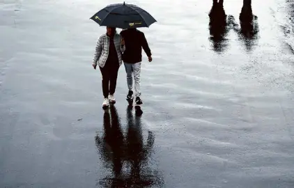  ?? Scott Strazzante/The Chronicle ?? A couple walks under an umbrella at Pier 39. A warmer world is making worse storms more likely.