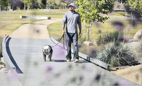  ?? Glenn Koenig Los Angeles Times ?? CHRIS EVERETT and his dog, Jack, cross a wooden bridge over a dry arroyo at Los Angeles State Historic Park. State lawmakers are negotiatin­g a measure that, if approved by voters next year, would spend billions to build and maintain parks and water...