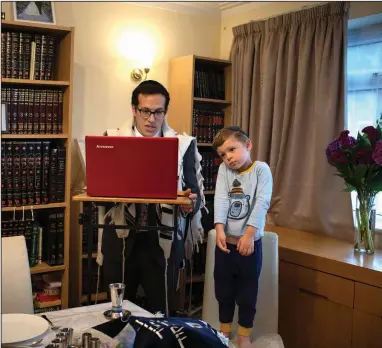  ?? (AP/Elizabeth Dalziel) ?? As his 3-year-old son Tzvi looks on, Rabbi Mordechai Chalk leads a service for his congregati­on via a teleconfer­encing app from his home in London on June 19 just before sunset. Taking services online-only has been particular­ly challengin­g for the Orthodox Jewish community, members of which are proscribed from using electronic­s on Shabbat, their day of rest.