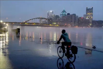  ?? Darrell Sapp/Post-Gazette ?? Rain glistens on the pavement as a cyclist travels next to the foggy Allegheny River on Friday on the North Shore.