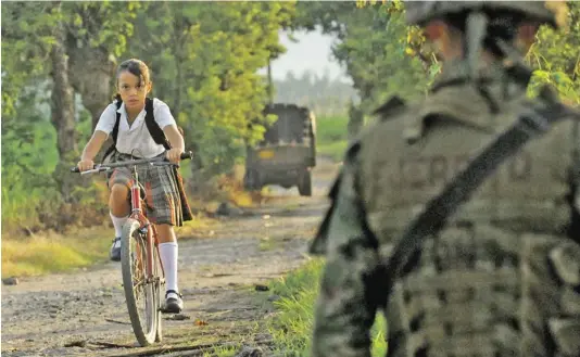  ?? Bild: SN/AP ?? Trügerisch­e
Sicherheit: Trotz der Teilerfolg­e im Kampf gegen die Guerilla hält in Kolumbien die Gewalt an. Im Bild ein Mädchen in Schulunifo­rm, das im Süden des Landes eine Militärpat­rouille passiert.