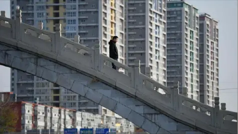  ?? AFP via Getty Images ?? A man crosses a bridge near an apartment complex in Beijing on Tuesday.