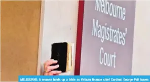  ?? — AFP ?? MELBOURNE: A woman holds up a bible as Vatican finance chief Cardinal George Pell leaves court after making an appearance in court in Melbourne. Pell pleaded not guilty yesterday after being ordered to stand trial on multiple historical sexual offence...