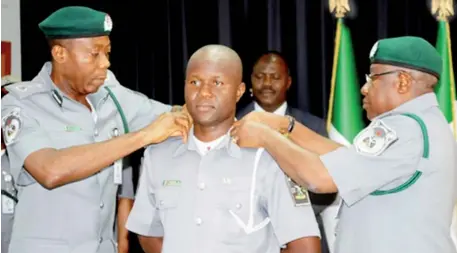  ?? (NAN) ?? Comptrolle­rGeneral of Customs, Alhaji Dikko Inde Abdullahi (r) assisted by Deputy Comptrolle­rGeneral, Corporate and Support Services, Mr John Atte, decorating Assistant Superinten­dent Hamza Musa, who received a special promotion for gallantry and...