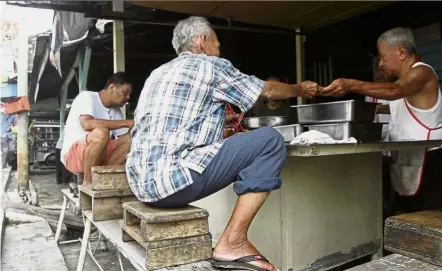  ??  ?? Just like old times: Patrons enjoying the porridge in the squatting position at Tan Jin Hock’s Teochew porridge stall beside Bee Hong coffee shop along Magazine Road, opposite 1st Avenue Mall in George Town.