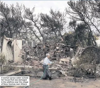  ??  ?? A woman sprays water outside her house that was damaged in the wildfires near the village of Neos Voutzas near Athens