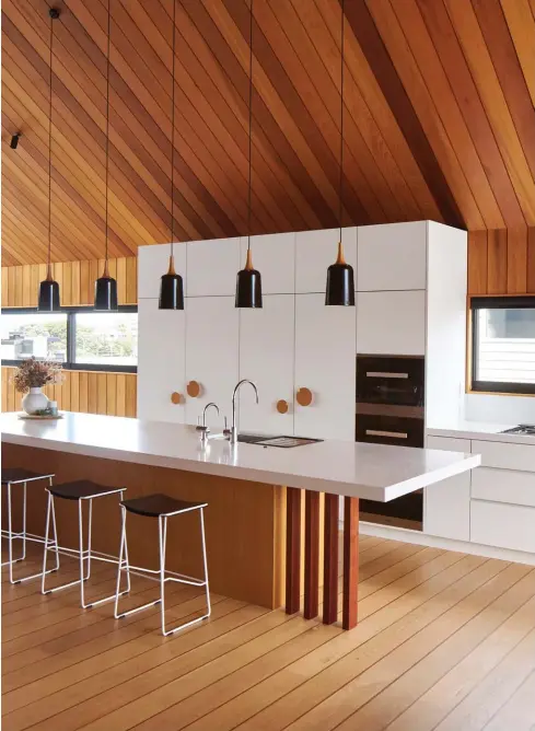  ??  ?? ABOVE & OPPOSITE, TOP RIGHT Ampel pendants designed by Tim light the generous kitchen island, underneath which the floor is in American oak, with kwila inserts to match the negative detail of the western red cedar ceiling and walls. The kitchen’s back bench extends into a dedicated coffee zone; the family enjoy their brews at the dining table or meander outside through the APL Architectu­ral Series sliding doors to sip them in the sun.